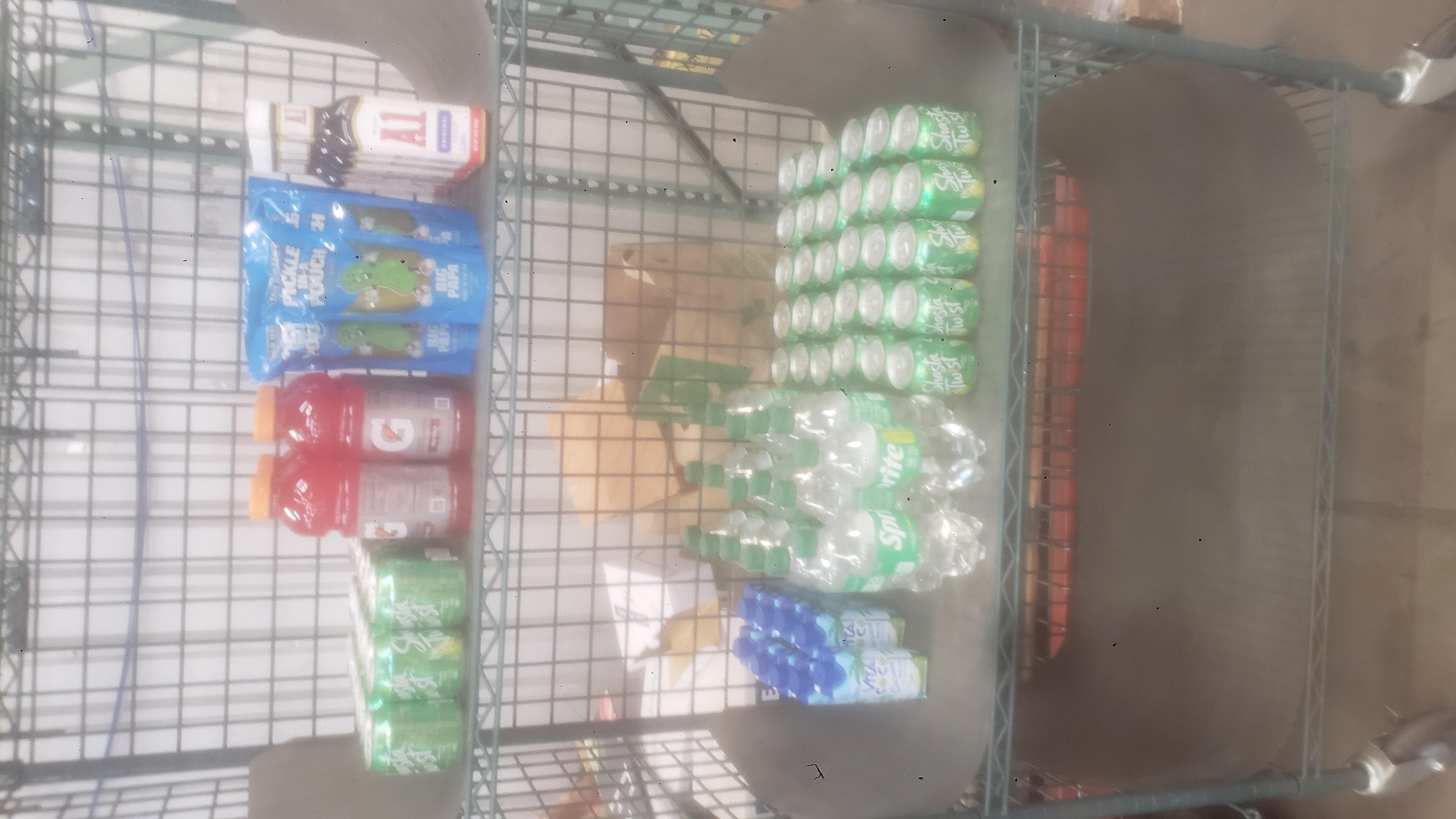 Cans of shasta twist, bottles of gatorade, pouches of pickles, bottles of A1 sauce, bottles of sprite, and cartons of coconut water on a cage shelf.